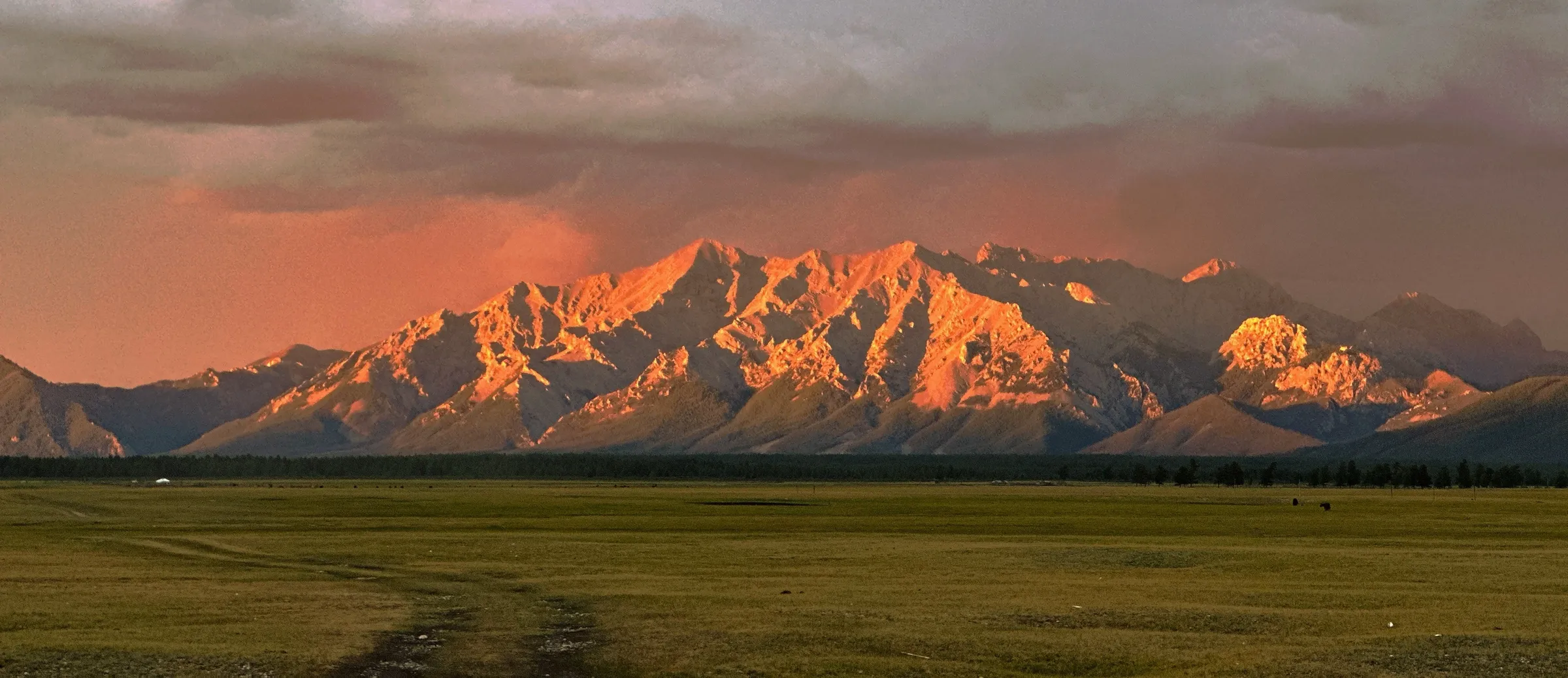 Alpenglow on a snow-streaked range above open steppe at dusk