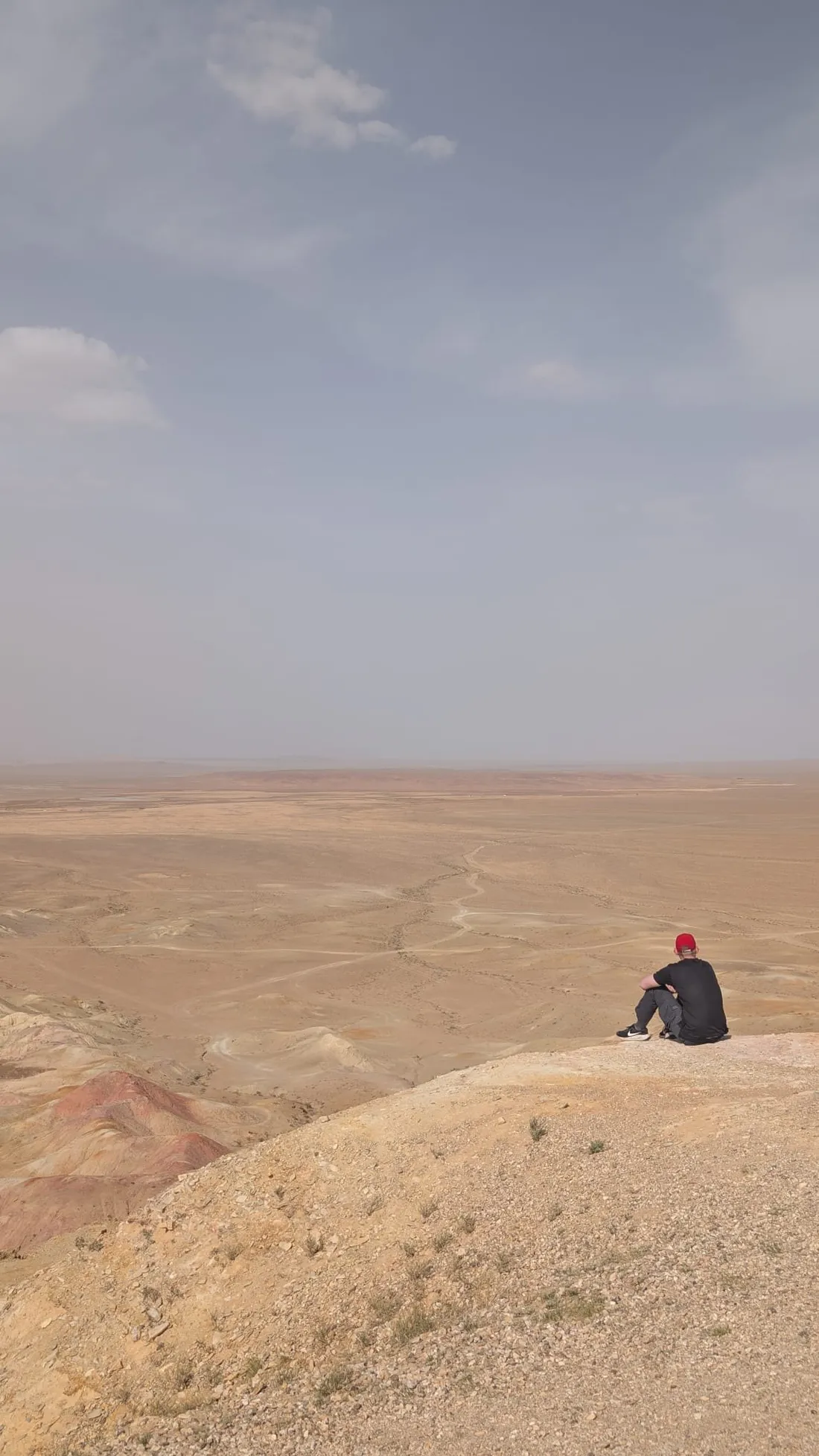 A lone figure seated on a cliff edge above the desert