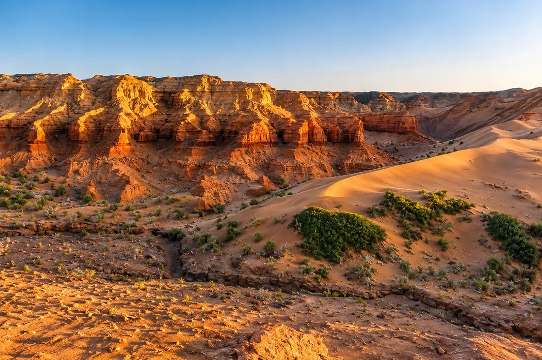 Eroded red cliffs and a sand dune lit by the low evening sun