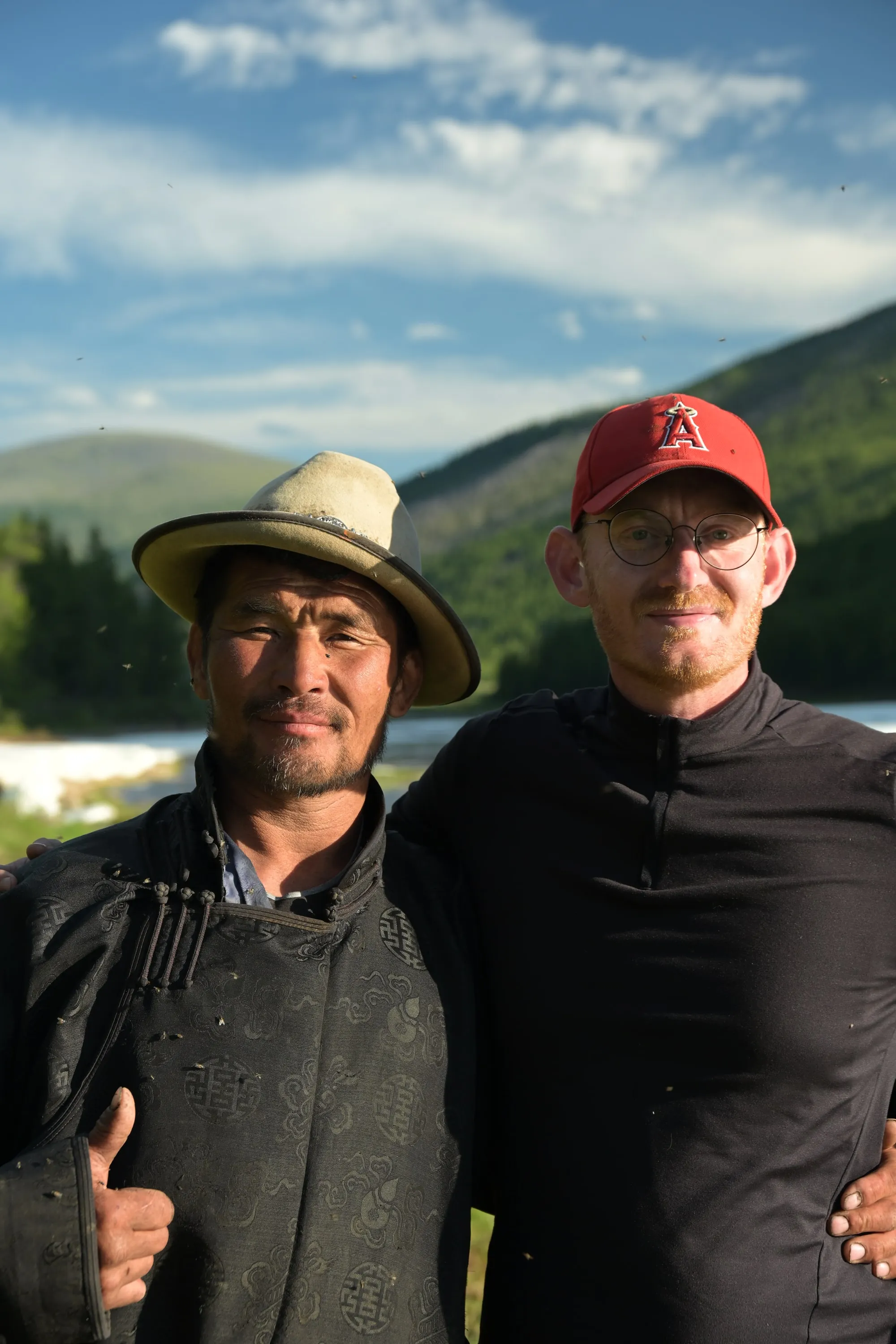 A herder and a traveller standing together above a river in the taiga