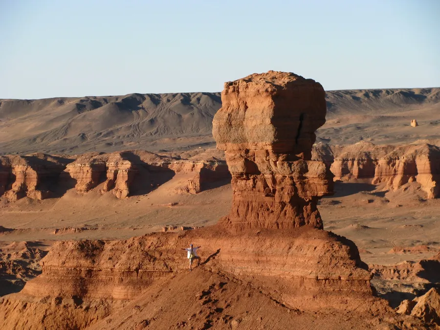 A tall red sandstone pillar among the canyons, with a walker at its foot