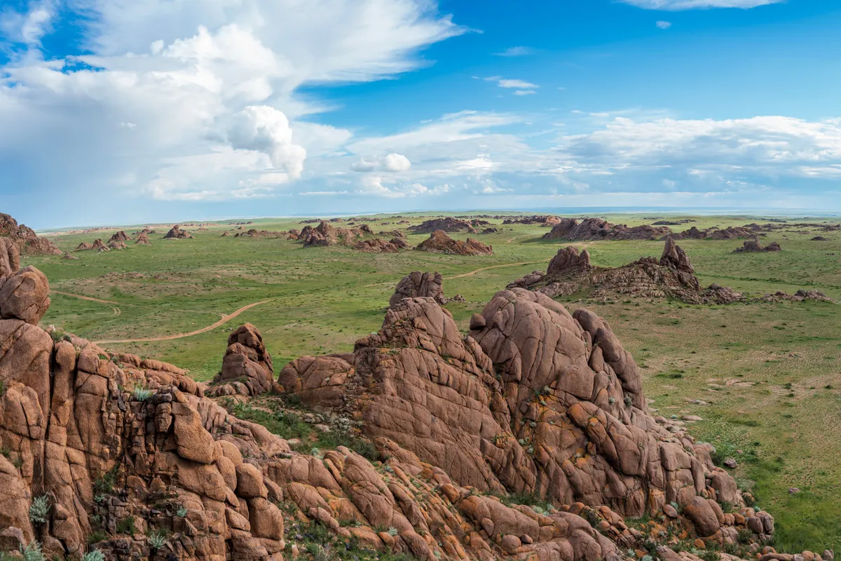 Granite outcrops rising from green plain at Ikh Gazriin Chuluu