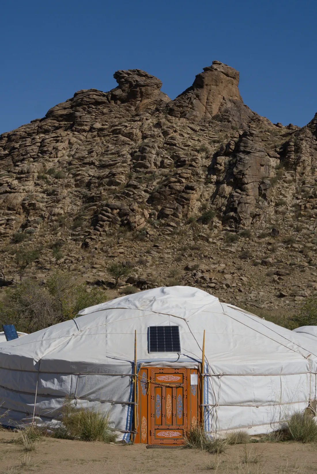 A ger with a painted orange door and a solar panel, standing below the granite outcrops of Ikh Nart