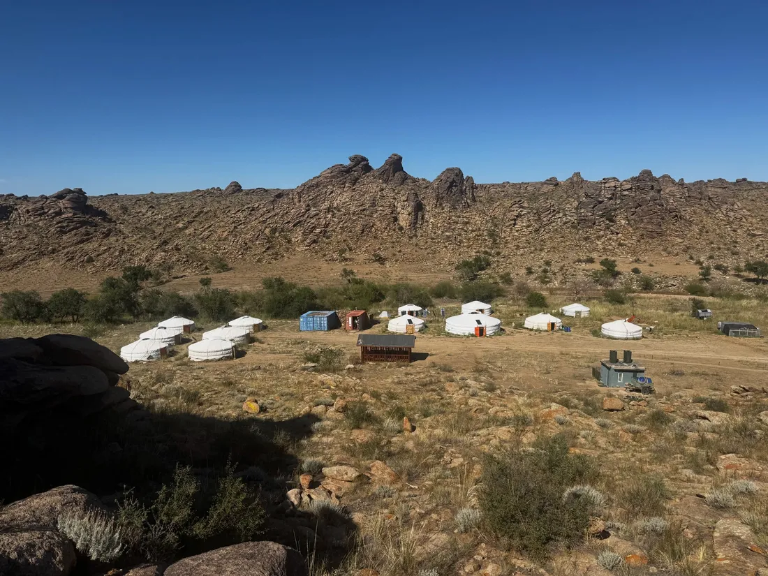 White gers of the Ikh Nart research camp spread across the steppe below a granite ridge