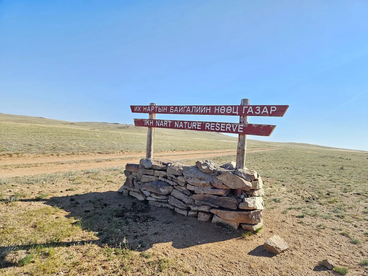 The Ikh Nart Nature Reserve sign, in Mongolian and English, on a dry-stone base beside a steppe track