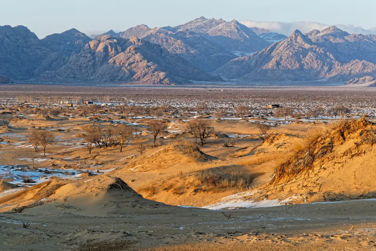 Snow-patched dunes below the rocky mountains of Khögnö Khan