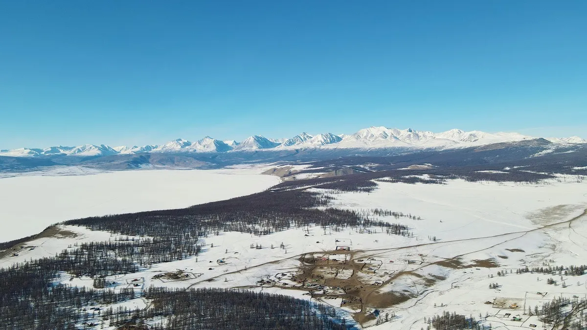 The frozen lake and a village on its shore, seen from above, with a snow range beyond