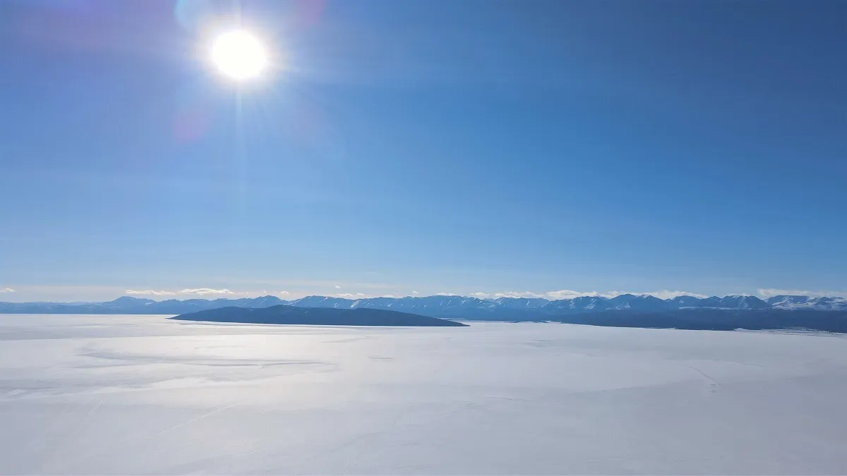 Low sun over the frozen surface of the lake, mountains along the far shore