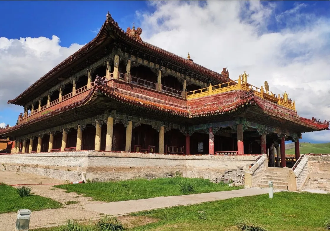 A large Buddhist temple with tiered roofs on a stone platform, green hills behind