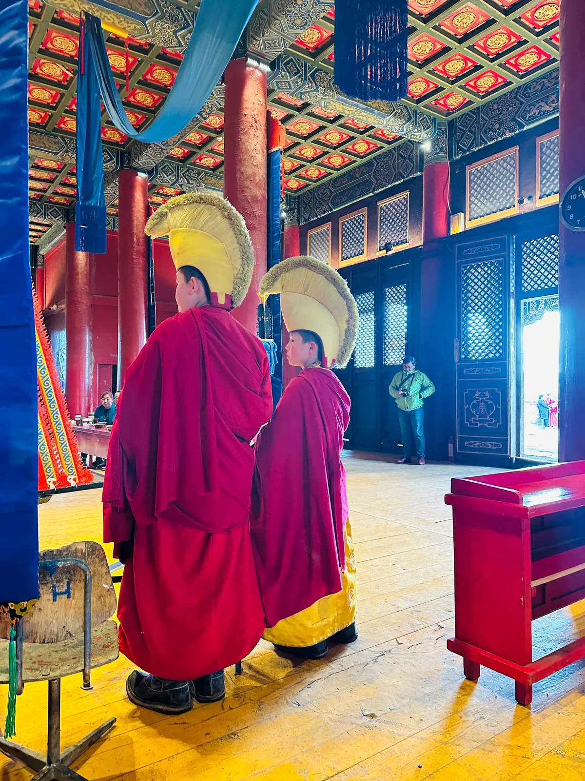 Two young monks in yellow crested hats inside a painted temple