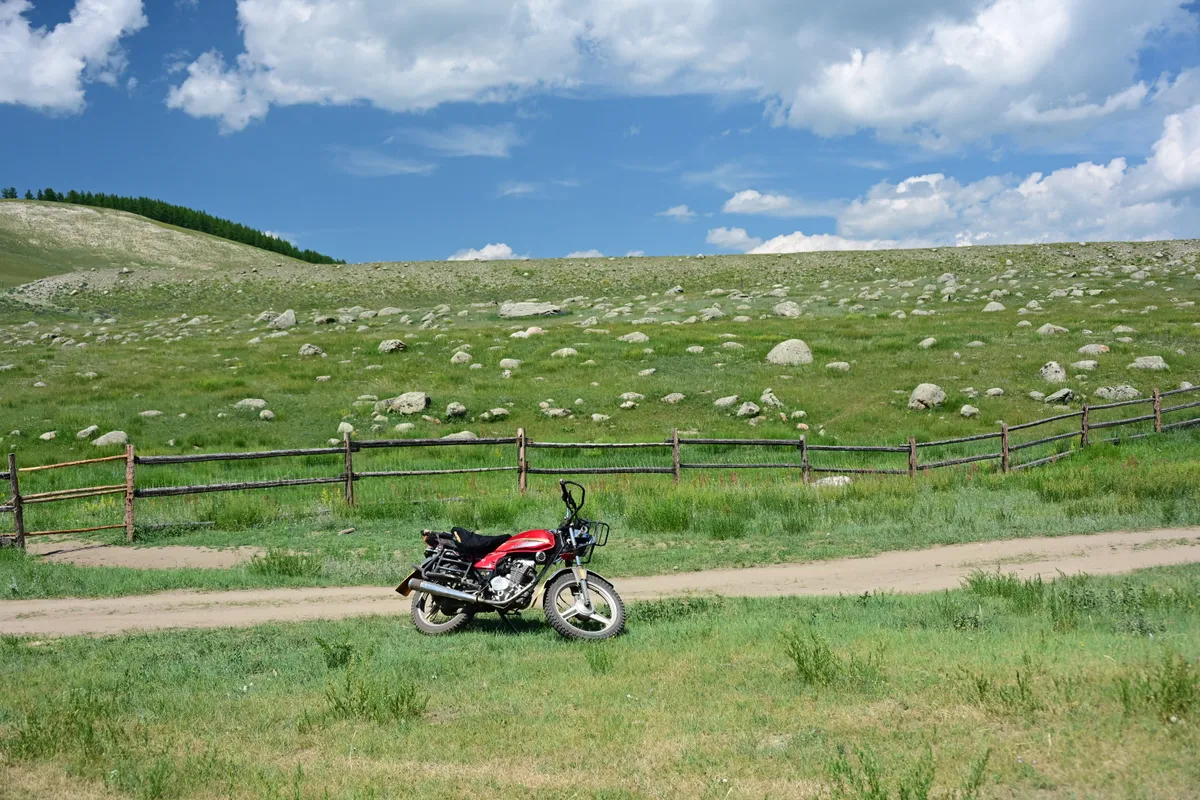 A motorbike parked on a track across a boulder-strewn green pasture