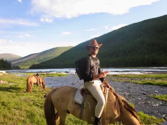 A rider in a wide-brimmed hat beside a braided taiga river