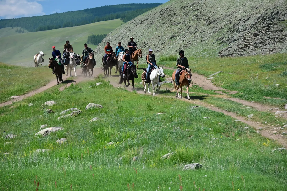 A column of riders and pack horses on a trail below a scree slope