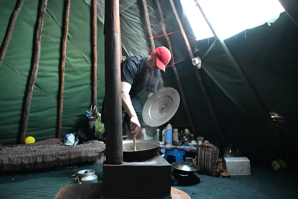 A man cooking on the stove inside a canvas teepee