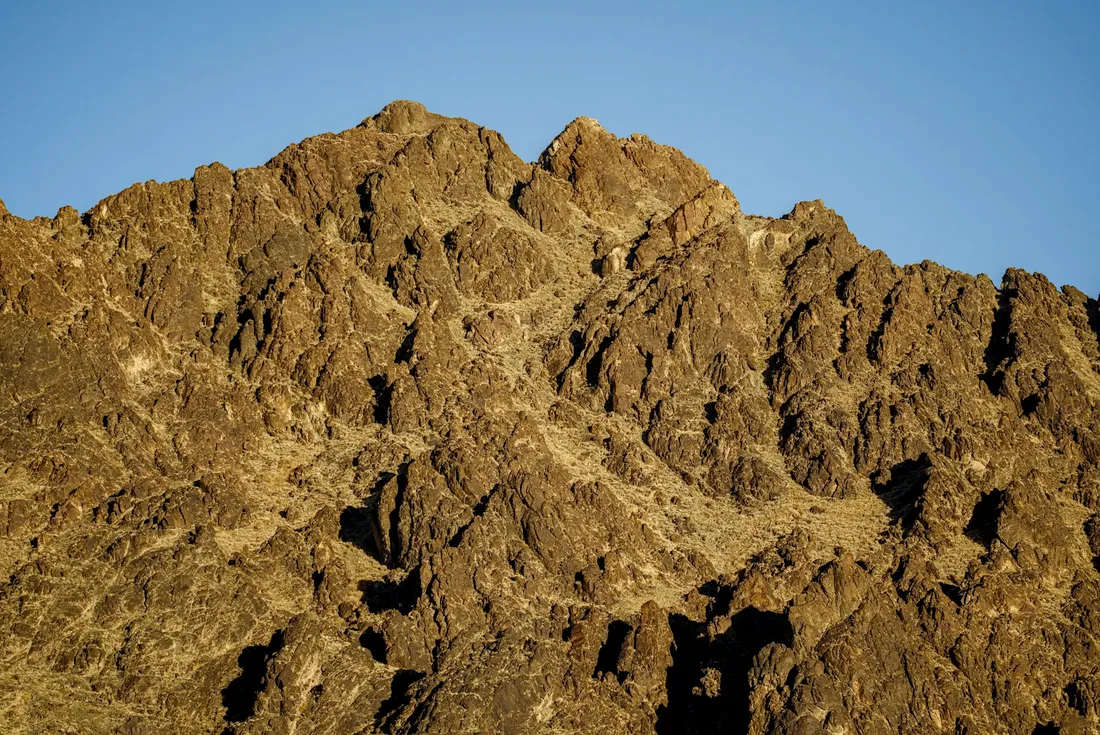 A rugged peak lit golden by the sun against a blue sky