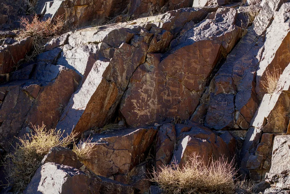 Ancient rock carvings on a dark rock face in the Tost Mountains.