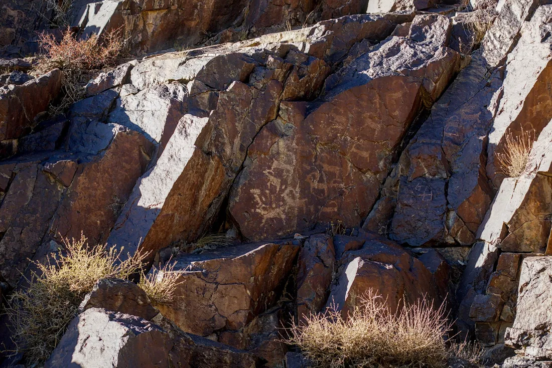 Ancient rock carvings on a dark rock face in the Tost Mountains