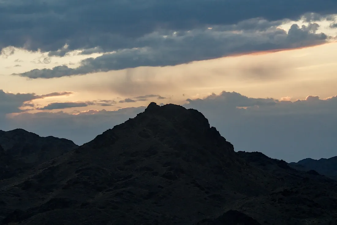 A dark mountain silhouetted against a sunset sky streaked with cloud