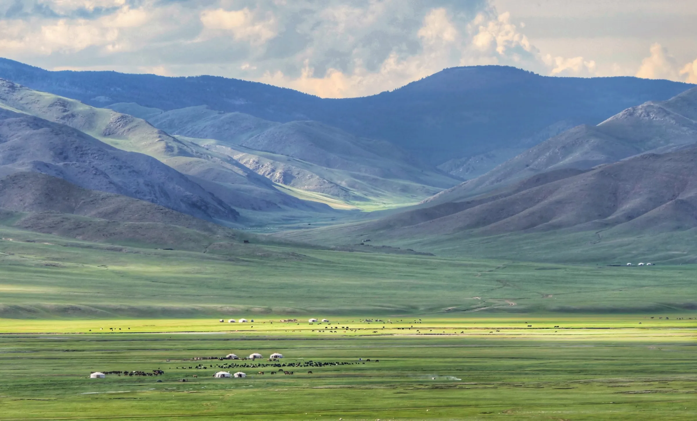 Layered ridges above a valley floor scattered with gers and grazing animals
