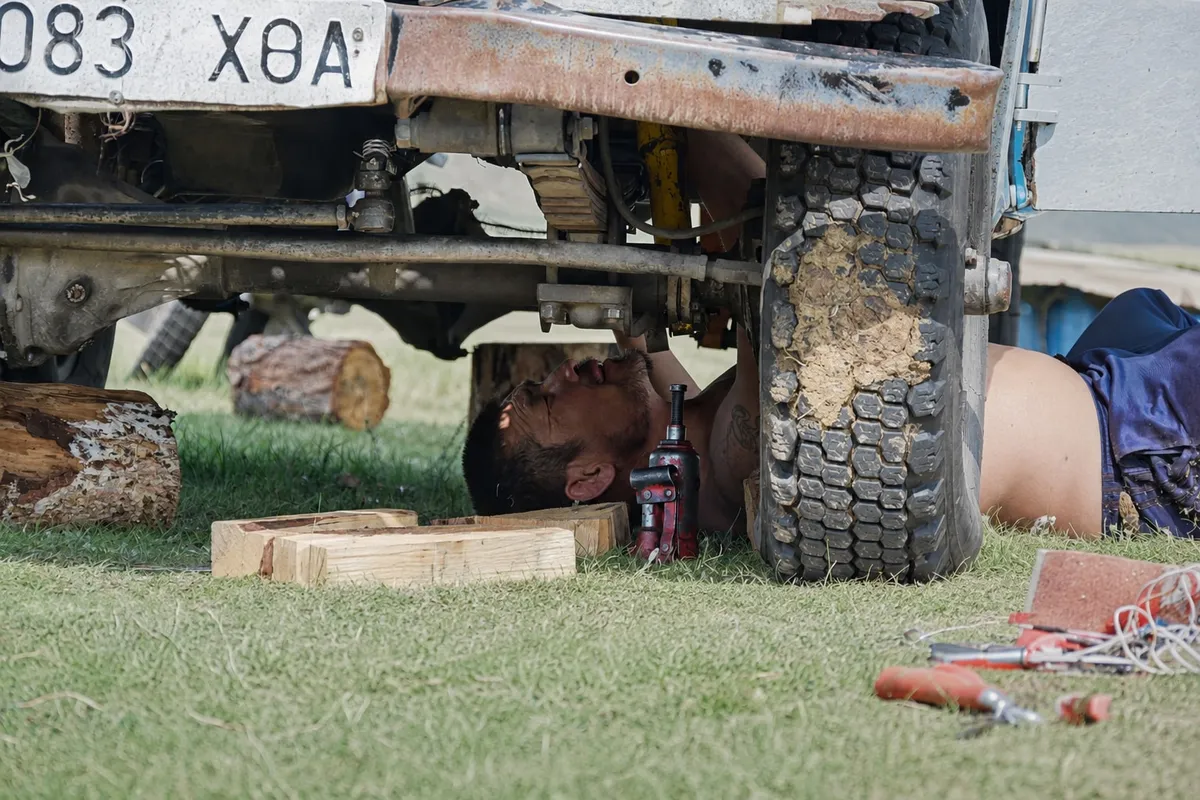 A driver lying under a van on a jack, working on the axle