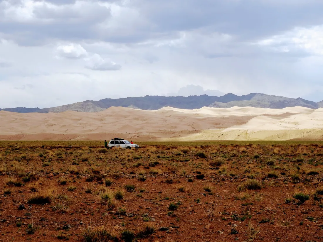 A vehicle parked on the plain before a dune field