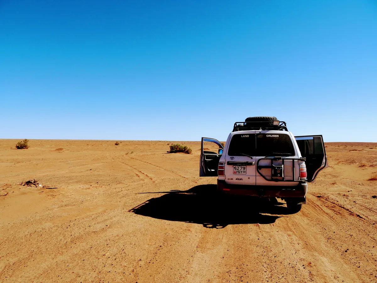 A four-wheel drive stopped on a desert track under an empty sky