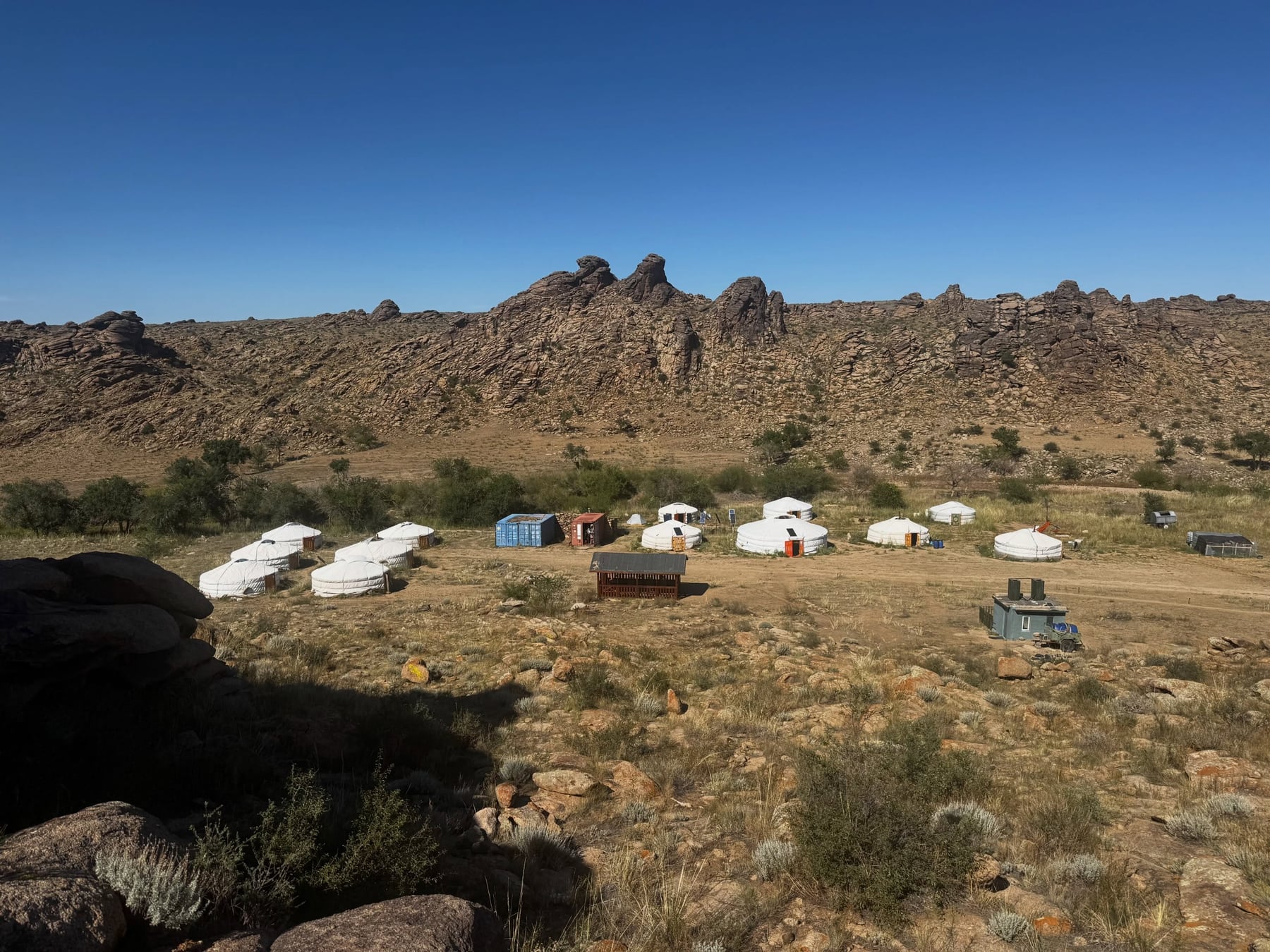 White gers of the Ikh Nart research camp spread across the steppe below a granite ridge